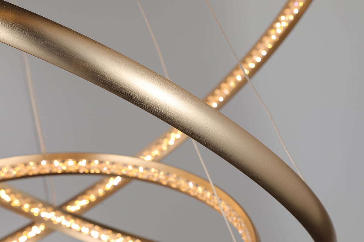 Złota lampa wisząca Brighton LED 3-punktowa, z trzema okrągłymi pierścieniami. Wykonana z metalowego materiału, z delikatnym, matowym wykończeniem. Widoczne diody LED wzdłuż krawędzi, zawieszona na cienkich linkach, w kształcie dynamicznej kompozycji.