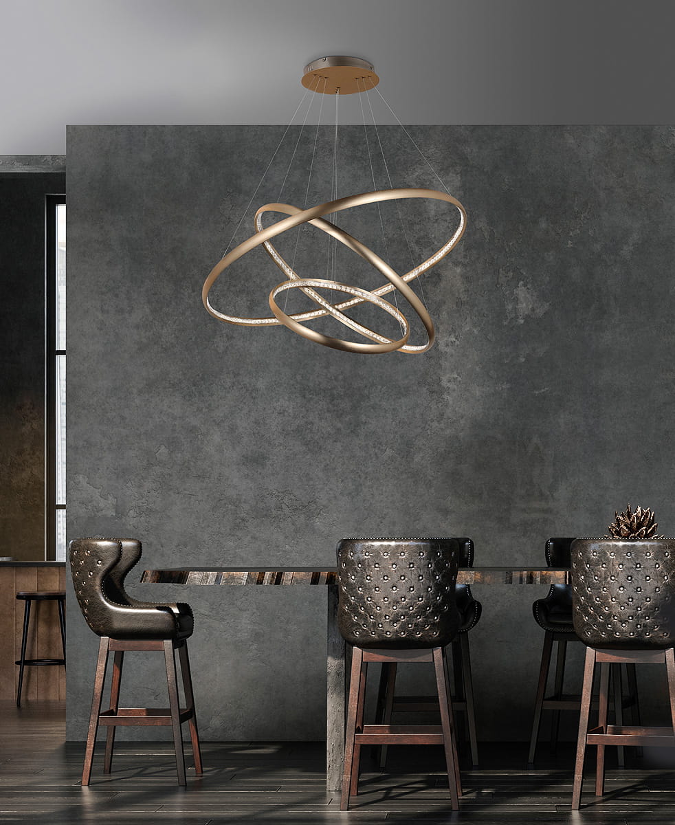 Złota lampa wisząca Brighton LED z trzema okręgami, zawieszona na cienkich linkach. Lampa umieszczona w nowoczesnym wnętrzu z szarymi ścianami i drewnianym stołem, otoczona przez ciemne krzesła barowe.