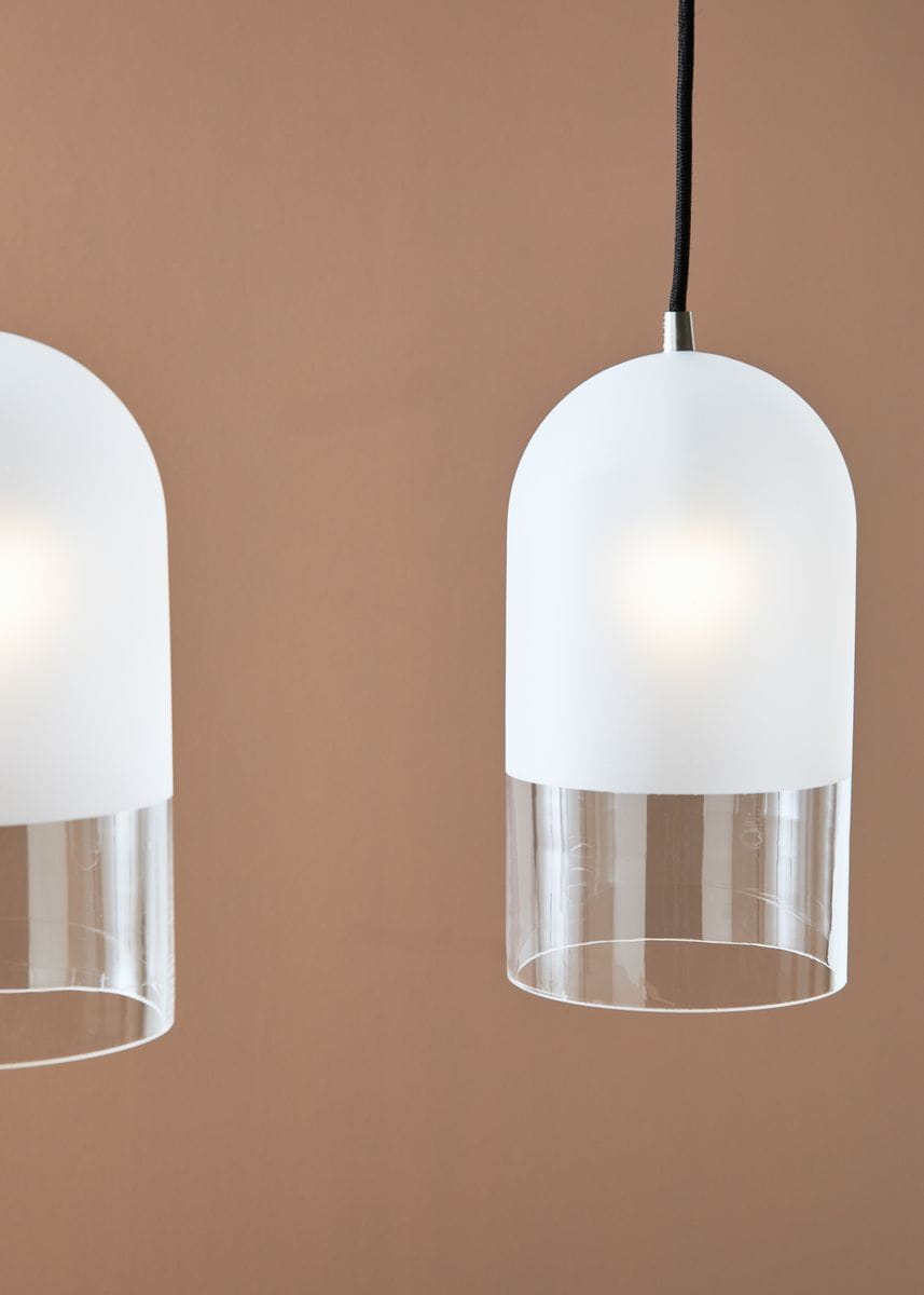 Czarna lampa wisząca Cope 3-punktowa z białymi kloszami o kształcie półkulistym, zdobionymi przezroczystym dnem. Ujęcie frontalne, zawieszona na czarnym przewodzie, w tle brązowa ściana. Idealna do nowoczesnych wnętrz.