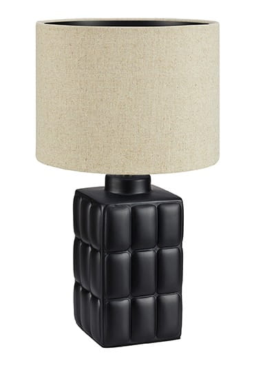 Lampa stołowa Cuscini Small, 1-punktowa. Czarna podstawka z fakturą w postaci kwadratowych wgłębień, z beżowym abażurem z materiału. Ujęcie frontalne, stojąca na płaskiej powierzchni.