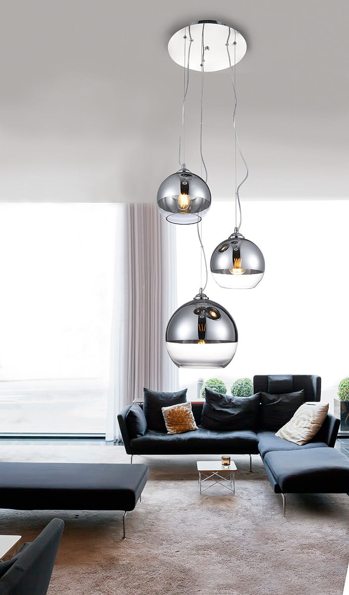 Lampa wisząca Silver Ball 3-punktowa AZ4750 z trzema chromowanymi kulami, zawieszona na długich kablach. Kule mają połyskliwą powierzchnię, a jedna z nich jest lekko przezroczysta. Lampa wisząca umieszczona w nowoczesnym wnętrzu z sofą i dużym oknem.
