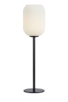 Cava lampa stołowa 1-punktowa w czarnej podstawie z białym, teksturowanym kloszem w kształcie walca. Lampa stoi na okrągłej podstawie, o delikatnej, nowoczesnej formie. Widoczna struktura klosza dodaje elegancji.