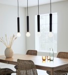 Czarna lampa wisząca Sencillo z czterema punktami świetlnymi, zawieszona w linii nad drewnianym stołem. Okrągłe, białe klosze w metalowych oprawach. W tle duże okno i dekoracje w wazonie.