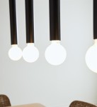 Czarna lampa wisząca Sencillo z czterema punktami świetlnymi. Długie, proste ramiona z matowego metalu, zawieszające białe, okrągłe żarówki. Ujęcie z bliska, na jasnym tle, podkreślające minimalistyczny design i nowoczesny styl.