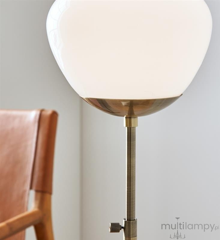 Lampa stołowa Rise 1-punktowa w antycznym mosiądzu z białym kloszem w kształcie kuli. Widok z boku, z widoczną regulacją wysokości i detalami metalowymi. Tło jasne, w tle fragment skórzowego krzesła.
