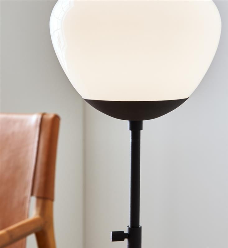 Lampa stołowa Rise 1-punktowa w kolorze czarnym i białym. Okrągła, matowa klosz z białego szkła na czarnym stelażu, z widocznym regulatorem na nodze. Ujęcie z boku, w tle widoczny fragment drewnianego krzesła.