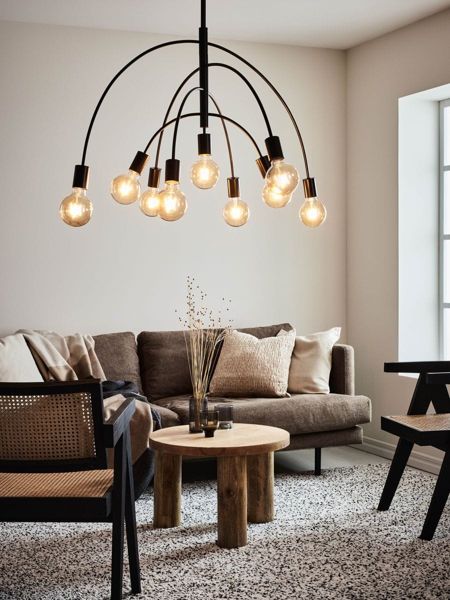 Lampa wisząca Lavello 9-punktowa w kolorze czarnym, z ośmioma zaokrąglonymi kloszami, zawieszona na cienkich, łukowatych ramionach. Widoczna w aranżacji wnętrza z sofą, stolikiem i dekoracjami. Tło jasne, minimalistyczne.