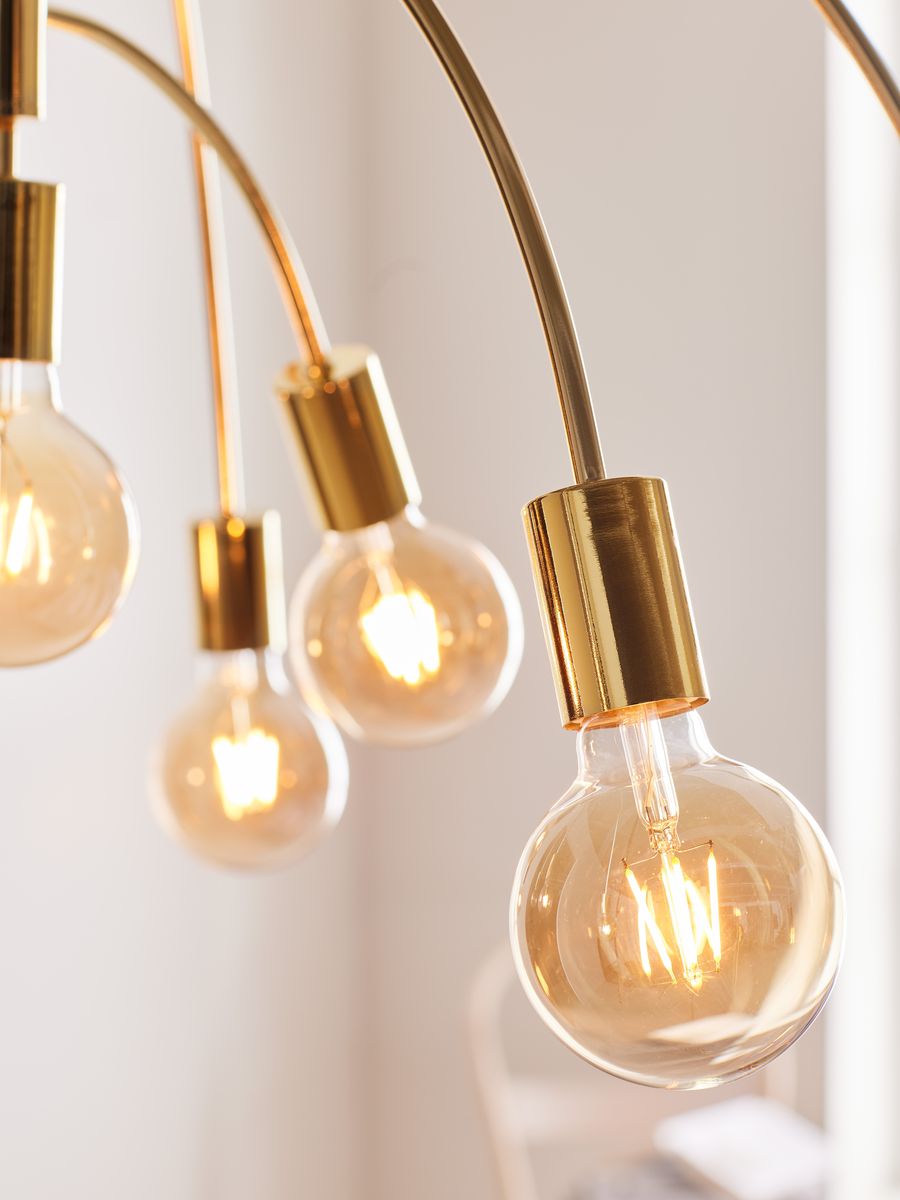 Lampa wisząca Lavello z dziewięcioma punktami świetlnymi, wykonana z mosiądzu. Widoczne szklane kule z żarówkami, elegancko zakrzywione ramiona. Tło jasne, minimalistyczne.