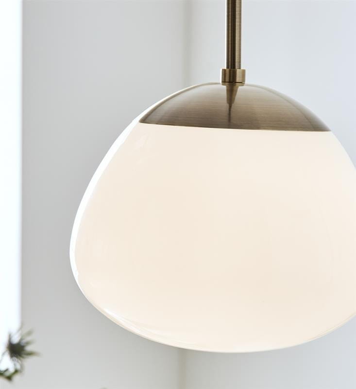Lampa wisząca Rise 1-punktowa w antycznym mosiądzu z białym kloszem o organicznym kształcie. Ujęcie zbliżeniowe, pokazujące detal klosza i mocowanie. Tło jasne, minimalistyczne.