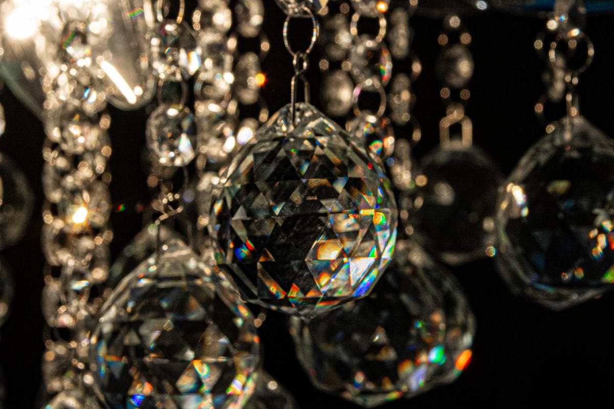 Lampa sufitowa Wenecja 4-punktowa w chromowanej oprawie, z kryształowymi dekoracjami w kształcie diamentów, zawieszonymi na metalowych łańcuszkach, odbijającymi światło w różnych kolorach. Ujęcie z bliska, podkreślające detale kryształów.