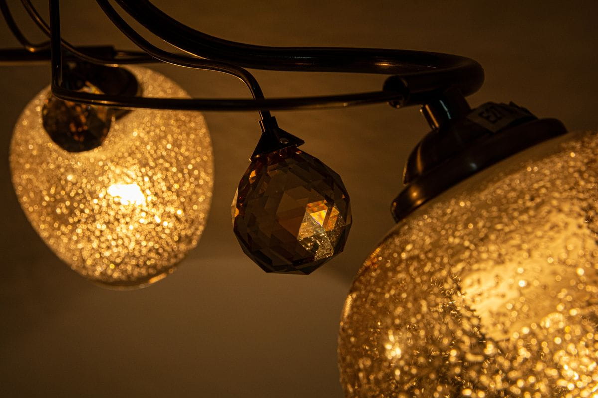 Lampa sufitowa Blanka 3-punktowa w kolorze patyny, z przezroczystymi kloszami o fakturze z drobnymi bąbelkami. Widoczne kryształowe zawieszenie w kształcie diamentu. Kąt ujęcia zbliżony, ukazujący detale i źródła światła.