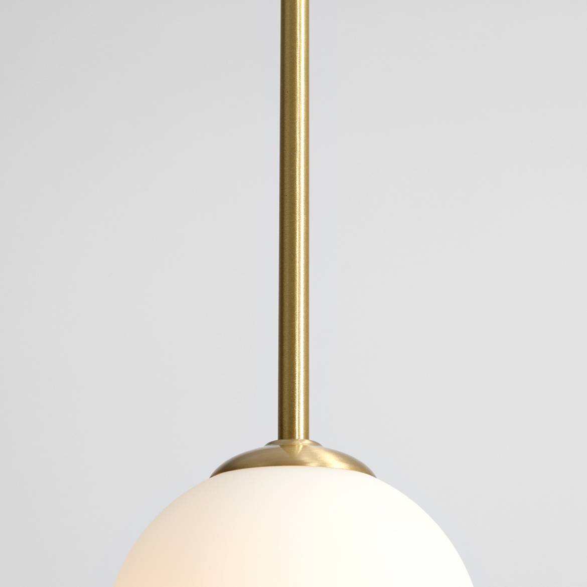 Lampa wisząca Bosso D30 w kolorze mosiężnym z okrągłym, matowym kloszem. Produkt zawieszony na cienkim, metalowym wysięgniku. Tło jasnoszare, podkreślające elegancki design lampy.