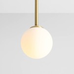 Lampa wisząca Pinne Short w kolorze mosiądzu z jednopunktowym zawieszeniem. Okrągła, matowa kula z białego szkła, zawieszona na cienkim mosiężnym pręcie. Tło jasne, jednolite.