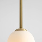 Lampa wisząca Pinne Medium w kolorze mosiądzu, z okrągłym kloszem z matowego szkła. Produkt pokazany z góry, zawieszony na cienkiej, metalowej rurce. Idealna do nowoczesnych wnętrz.
