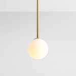 Lampa wisząca Pinne Long w kolorze mosiądzu z pojedynczym punktem świetlnym. Na długim, prostym zawieszeniu wisi okrągła, mleczna kula. Produkt umieszczony na jednolitym tle.