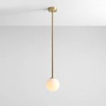 Lampa wisząca Pinne Long w kolorze mosiądzu, z pojedynczym źródłem światła, zawieszona na długim, prostym stelażu. Klosz w formie białej, półprzezroczystej kuli, umieszczony na dolnej części. Tło w jasnym kolorze.