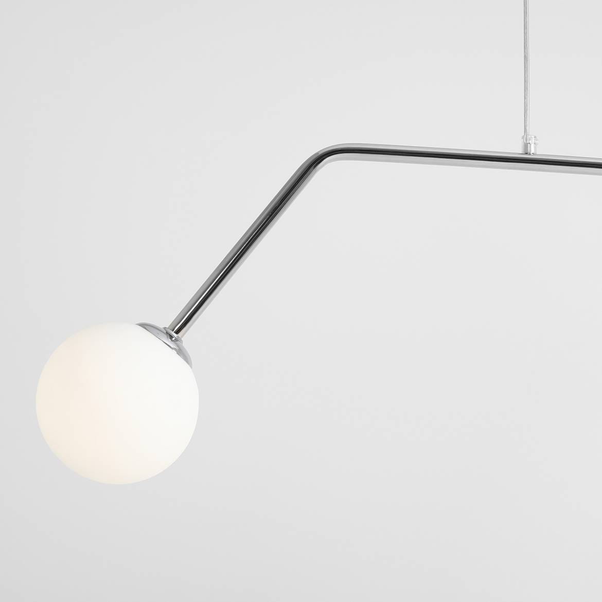 Lampa wisząca Pure 2-punktowa w kolorze chromu, z długim, zakrzywionym ramieniem. Na końcu znajduje się biała kula z matowego szkła. Produkt zawieszony na cienkim, metalowym przewodzie, na jasnym tle.