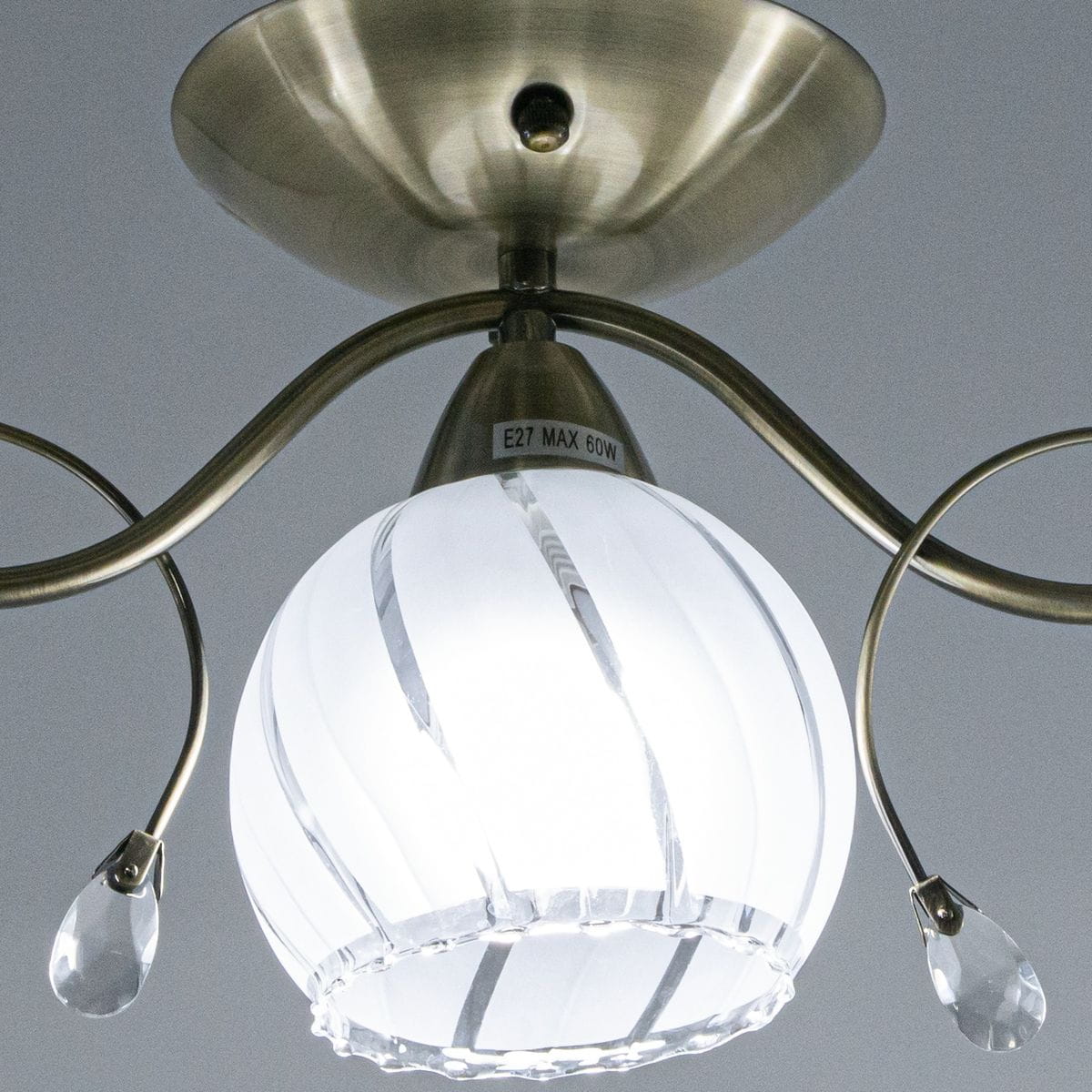 Lampa sufitowa Sting 3-punktowa w kolorze mosiądzu z białą, szklaną kloszem w kształcie kuli. Klosz zdobiony pionowymi żłobieniami i dekoracyjnymi kryształkami. Ujęcie z dołu, ukazujące mocowanie oraz elementy dekoracyjne.