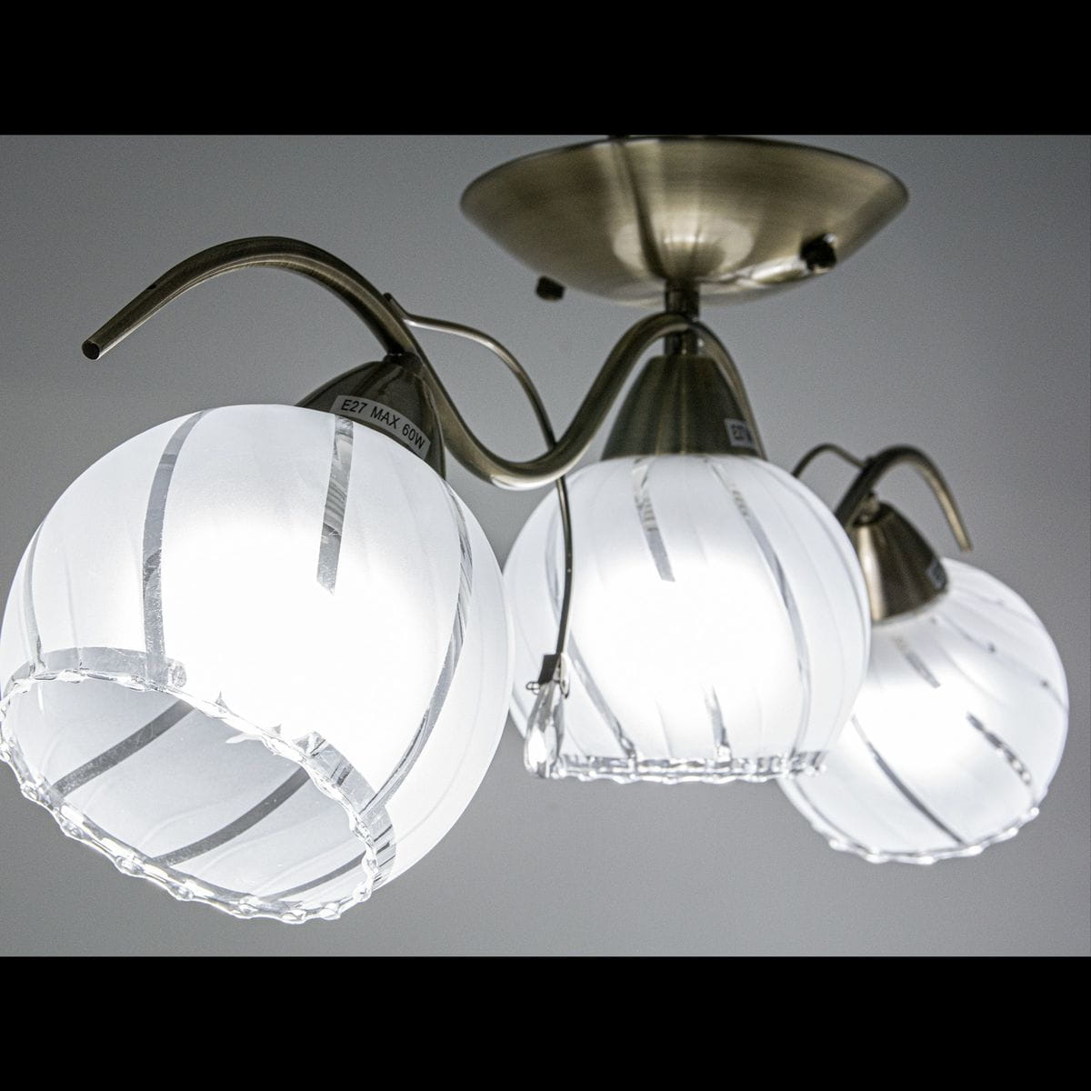 Lampa sufitowa 3-punktowa w kolorze mosiądzu z trzema kulistymi kloszami ze szkła. Klosze mają białą powierzchnię z delikatnym wzorem i falistym brzegiem. Ujęcie z dołu, pokazujące zawieszenie i kształt lampy.