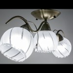 Lampa sufitowa 3-punktowa w kolorze mosiądzu z trzema kulistymi kloszami ze szkła. Klosze mają białą powierzchnię z delikatnym wzorem i falistym brzegiem. Ujęcie z dołu, pokazujące zawieszenie i kształt lampy.