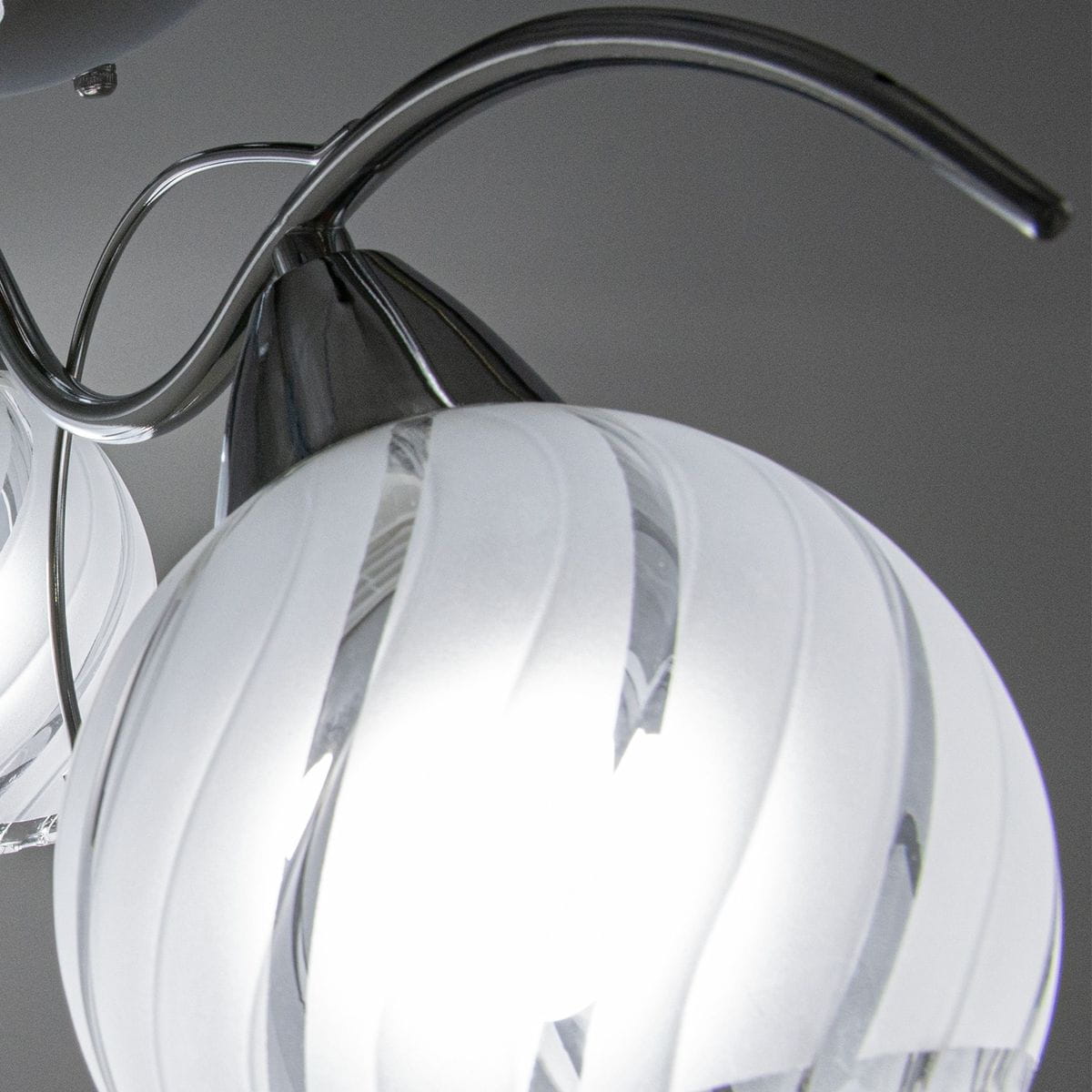 Lampa sufitowa 3-punktowa Sting w kolorze chromu. Szklane klosze o dekoracyjnej, spiralnej fakturze. Ujęcie z góry, skupione na detalach kloszy i metalowych elementów mocujących. Tło proste, szare.
