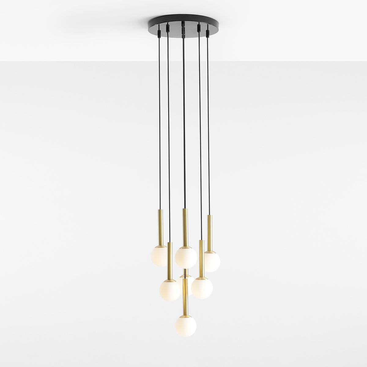 Lampa wisząca Riu 7-punktowa z czarnym stelażem i mosiężnymi detalami. Składa się z siedmiu białych, okrągłych kloszy zawieszonych na czarnych linkach. Montowana sufitowo, w minimalistycznym stylu, na jasnym tle.