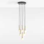 Lampa wisząca Riu 7-punktowa z czarnym stelażem i mosiężnymi detalami. Składa się z siedmiu białych, okrągłych kloszy zawieszonych na czarnych linkach. Montowana sufitowo, w minimalistycznym stylu, na jasnym tle.