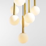 Lampa wisząca Riu 7-punktowa w kolorze czarnym i mosiądzu, z sześcioma okrągłymi, matowymi kloszami w białym kolorze, zamontowana na metalowych prętach w odcieniu mosiądzu, zawieszona w pionie, na jasnym tle.