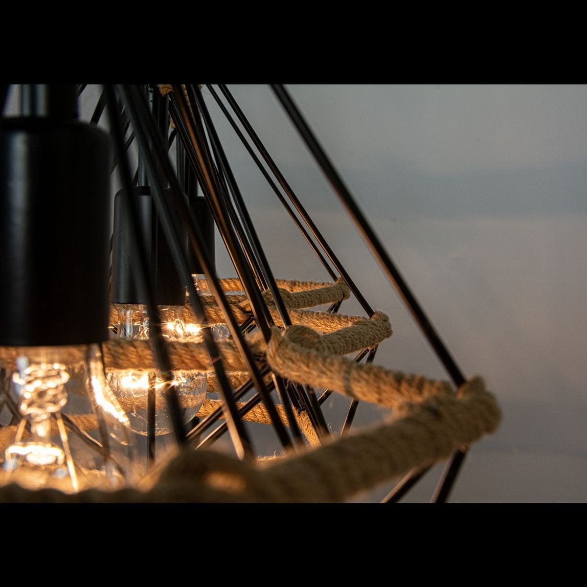 Lampa wisząca Piramida 3-punktowa w kolorze czarnym. Widoczne metalowe ramiona i sznur z juty. Ujęcie z bliska, ukazujące źródła światła oraz dekoracyjne elementy. Ciepłe światło podkreśla industrialny styl lampy.
