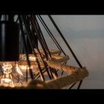 Lampa wisząca Piramida 3-punktowa w kolorze czarnym. Widoczne metalowe ramiona i sznur z juty. Ujęcie z bliska, ukazujące źródła światła oraz dekoracyjne elementy. Ciepłe światło podkreśla industrialny styl lampy.