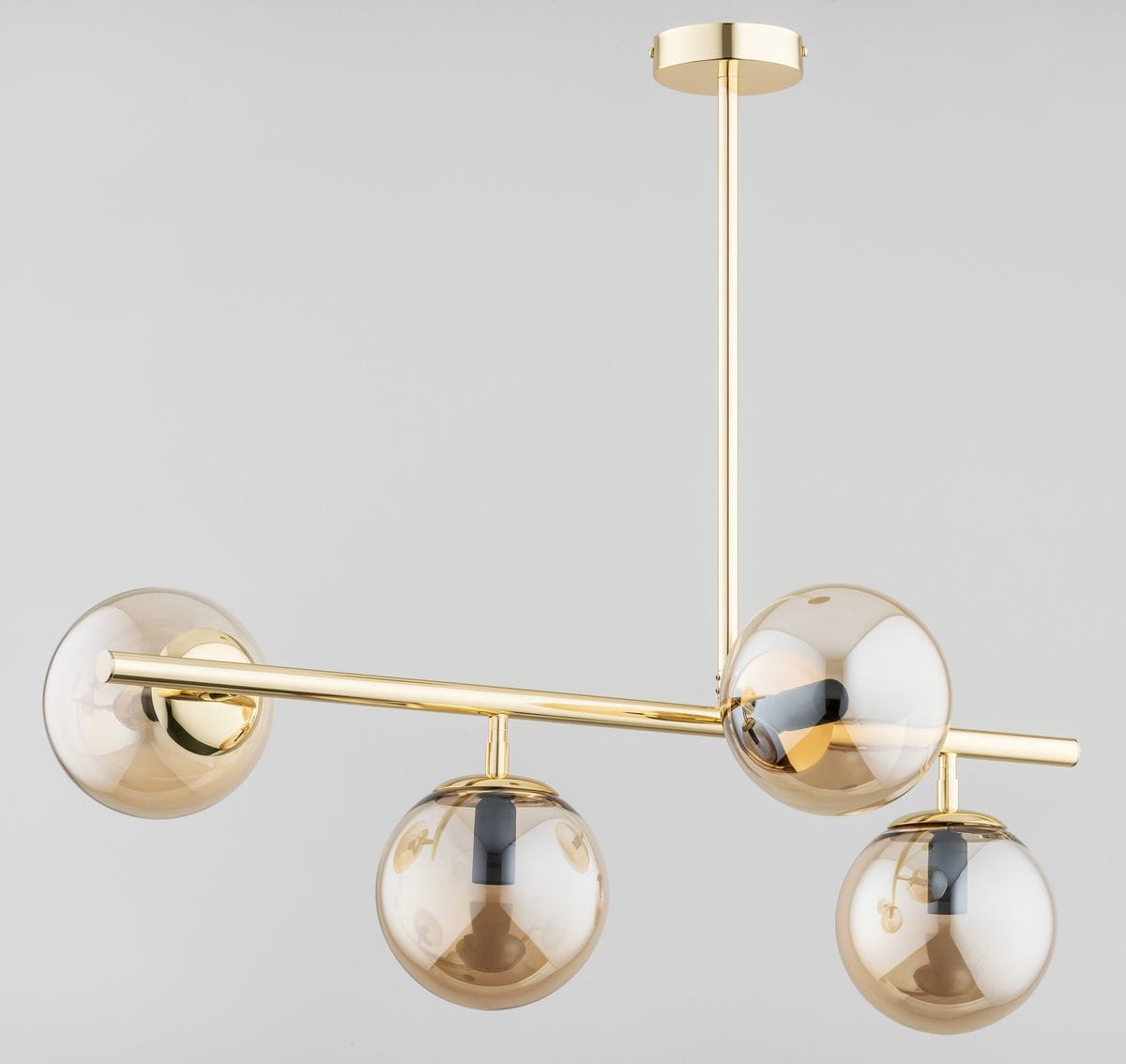 Lungo lampa wisząca 4-punktowa w kolorze złotym, z czterema szklanymi kulami w odcieniu brązowym. Produkt zawieszony na cienkim, złotym stelażu w prostokątnym kształcie, z góry widoczna okrągła podsufitka.