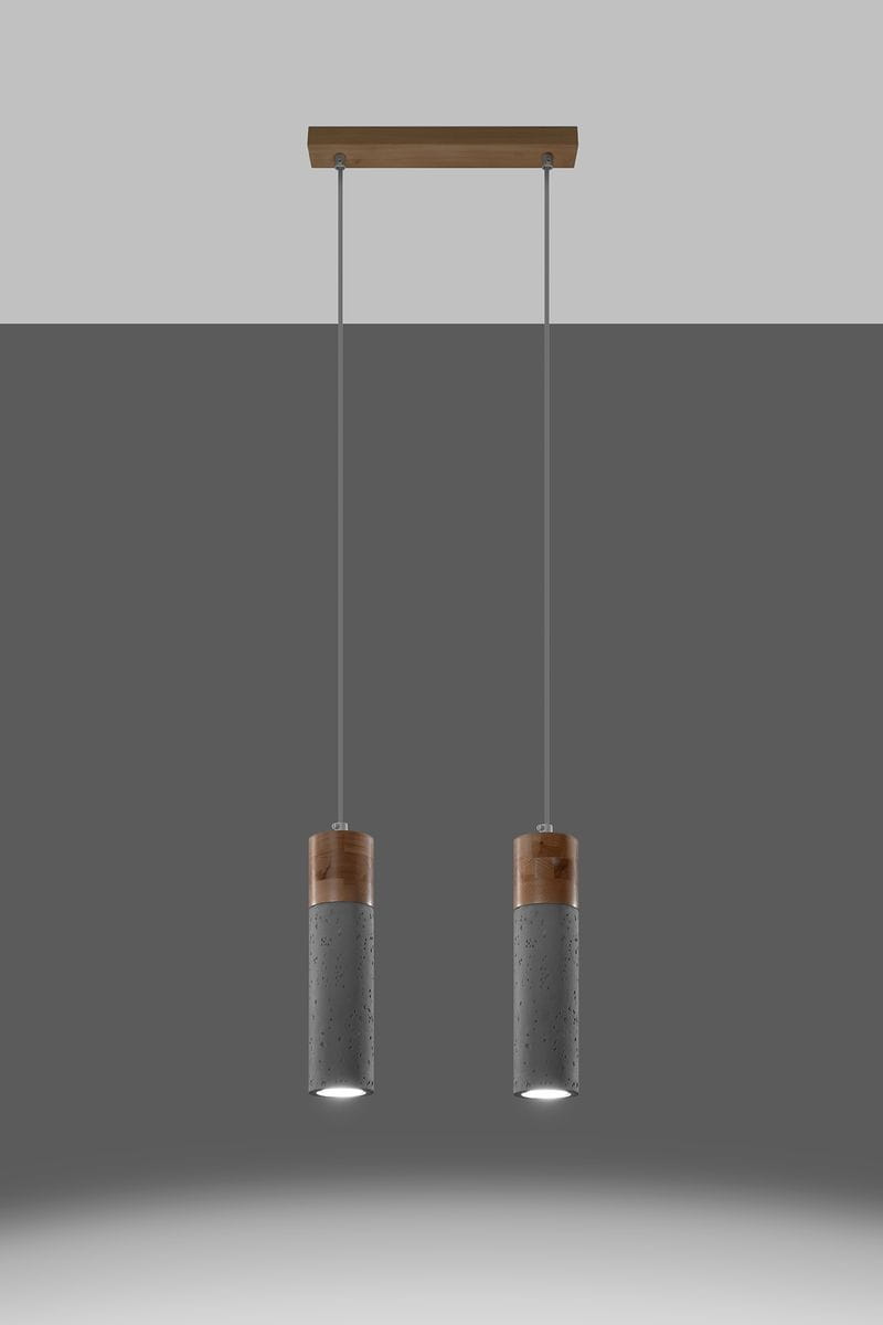 Lampa wisząca Zane 2-punktowa w kolorze szarym, z dwoma cylindrycznymi kloszami z betonu z drewnianymi detalami u góry. Utrzymana w formacie wiszącym, zawieszona na cienkich linkach, na jednolitym tle.