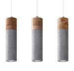 Lampa wisząca 3-punktowa Zane w szarym kolorze. Cylindryczne klosze z betonu z widocznymi teksturami, u góry drewniane wykończenie. Zawieszenie na białym przewodzie. Produkt w pozycji wiszącej, pokazany z przodu.