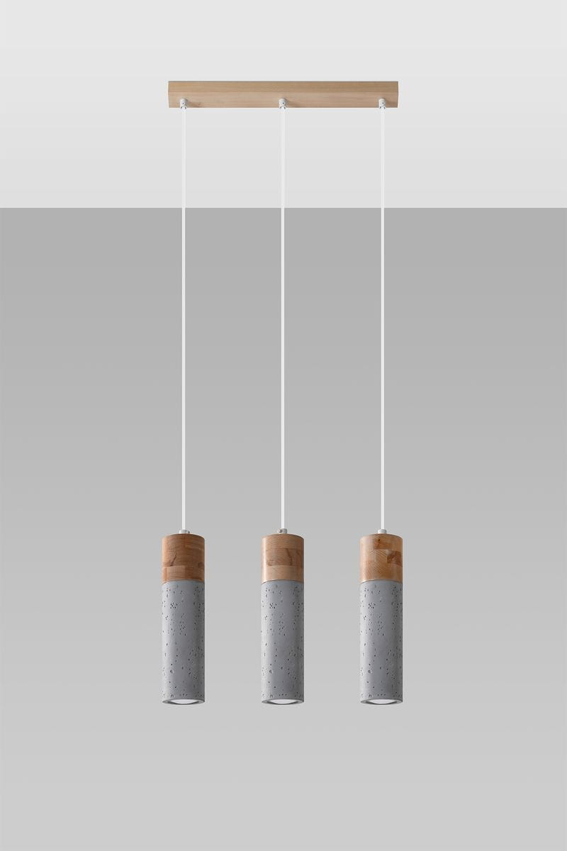 Lampa wisząca Zane 3-punktowa w kolorze szarym, składająca się z trzech cylindrycznych kloszy z betonu z drewnianymi elementami u góry. Zawieszona na białych linkach, umieszczona na drewnianej podstawie. Prosta, nowoczesna konstrukcja.
