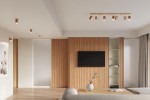Lampa sufitowa Zeke, 6-punktowa, w jasnym drewnie. Ujęcie frontalne, zamontowana na suficie. Żarówki w kształcie prostokątów, skierowane w różnych kierunkach. Tło w neutralnych barwach, minimalistyczne wnętrze z telewizorem na ścianie.