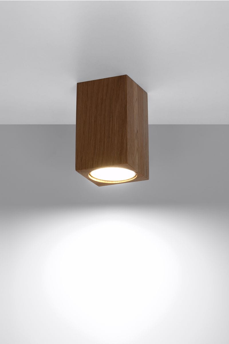 Lampa sufitowa Keke H10 w kolorze dębu, o prostokątnym kształcie, zamontowana na suficie. Emituje światło z okrągłego źródła, umieszczone w dolnej części obudowy. Tło jasne, co podkreśla naturalny wygląd drewna.