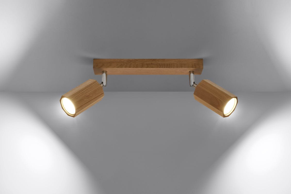 Lampa sufitowa Zeke 2-punktowa, z drewnianą, jasną podstawą i dwoma cylindrycznymi kloszami w odcieniu naturalnego drewna. Klosze są ruchome, zamontowane na chromowanych mocowaniach, emitując ciepłe światło na neutralnym tle.