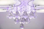 Lampa sufitowa Antila E27, 5-punktowa, w chromie z białą siatką. Zbliżenie na kryształowe dekoracje w kształcie diamentów, zawieszone na łańcuszkach, z podświetleniem w odcieniu fioletowym. Ujęcie z dołu, ukazujące szczegóły wykończenia.