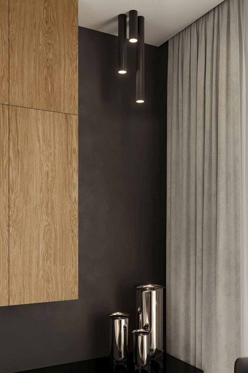 Czarna lampa sufitowa Lagos H10 z jedną oprawą, zawieszona w pionie. Wykonana z metalowego materiału, ma cylindryczny kształt. W tle widoczna drewniana szafka i szare zasłony. Elementy dekoracyjne w formie metalowych pojemników na blacie.