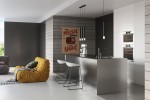 Czarna lampa wisząca Wezyr 1-punktowa, umieszczona nad kuchenną wyspą, w prostokątnym kształcie. Lampa ma metalowy klosz z przezroczystym elementem u dołu, zawieszona na cienkim przewodzie. W tle nowoczesne wnętrze z jasnymi i ciemnymi panelami.