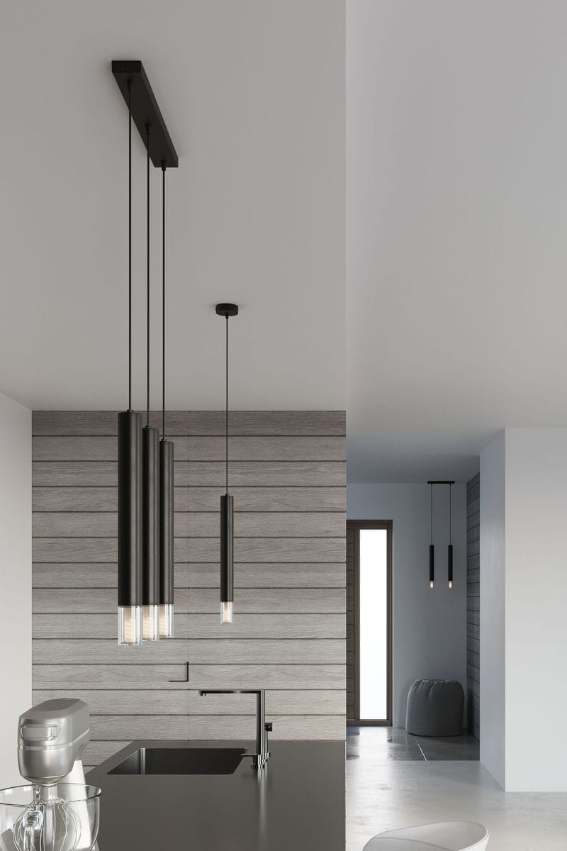 Czarna lampa wisząca Wezyr 3-punktowa, z trzema cylindrycznymi kloszami, zawieszona na długich przewodach. Ujęcie frontalne, w nowoczesnym wnętrzu kuchennym z drewnianą ścianą w tle. Widać także elementy wyposażenia kuchni, jak zlew i mikser.