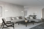 Kinkiet Tila 30 w kolorze białym, zamontowany na ścianie, o łagodnych kształtach. W tle nowoczesny salon z szarymi sofami, czarnym stolikiem i dekoracjami. Oświetlenie tworzy przytulną atmosferę w minimalistycznym wnętrzu.