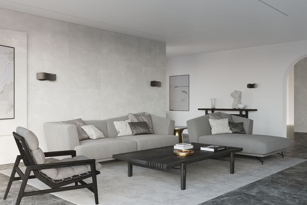 Kinkiet Tila 30 w kolorze czarnym, zamontowany na ścianie w nowoczesnym wnętrzu. Prosta, minimalistyczna forma z wykończeniem matowym. W tle widoczna szara sofa, stół oraz dekoracje w jasnych odcieniach.