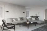 Kinkiet Tila 30 w kolorze czarnym, zamontowany na ścianie w nowoczesnym wnętrzu. Prosta, minimalistyczna forma z wykończeniem matowym. W tle widoczna szara sofa, stół oraz dekoracje w jasnych odcieniach.