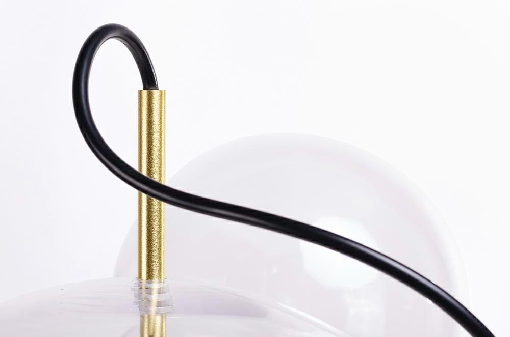 Lampa wisząca Capri LED z jedną punktową oprawą, złota metalowa podstawa z czarnym kablem. Widoczna część lampy z wykończeniem w kolorze złotym i przezroczystą kulistą kloszem. Ujęcie z góry, ukazujące detale konstrukcji.