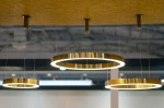 Lampa wisząca Ring D60 LED w kolorze złotym, z okrągłym kształtem i podświetleniem LED. Zawieszona na cienkich linkach, prezentuje minimalistyczny styl. Widoczna w aranżacji z innymi lampami tego samego typu, na tle jasnego sufitu.