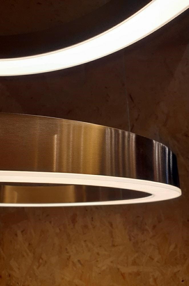 Lampa wisząca Ring D60 LED w złotym kolorze, z okrągłym kształtem i białym podświetleniem. Ujęcie z boku, ukazujące metaliczną teksturę oraz detale konstrukcji. Tło w neutralnym kolorze, eksponujące lampę.