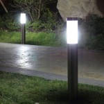 Okrągła lampa stojąca Manila H65 w kolorze srebrnym, umieszczona na ścieżce. Lampa ma szklany klosz emitujący jasne światło, z metalowym, polerowanym słupkiem. W tle widoczna trawa i krzewy, zdjęcie wykonane w nocy.