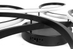 Czarna lampa sufitowa LED 100W z pilotem, składająca się z płaskiej podstawy i trzech zakrzywionych, białych pierścieni. Ujęcie z boku ukazuje detale mocowania i kształt konstrukcji. Tło proste, białe.