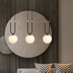 Lampa wisząca Glam 3-punktowa w kolorze czarnym i białym, z trzema okrągłymi kloszami z matowego szkła zawieszonymi na długich, czarnych kablach. Elementy metalowe w kolorze złotym. Tło w odcieniu drewna z dekoracyjnym okrągłym panelem.